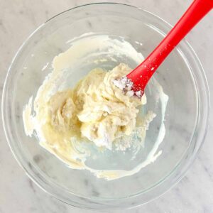 Combining cream cheese and powdered sugar in a glass bowl.