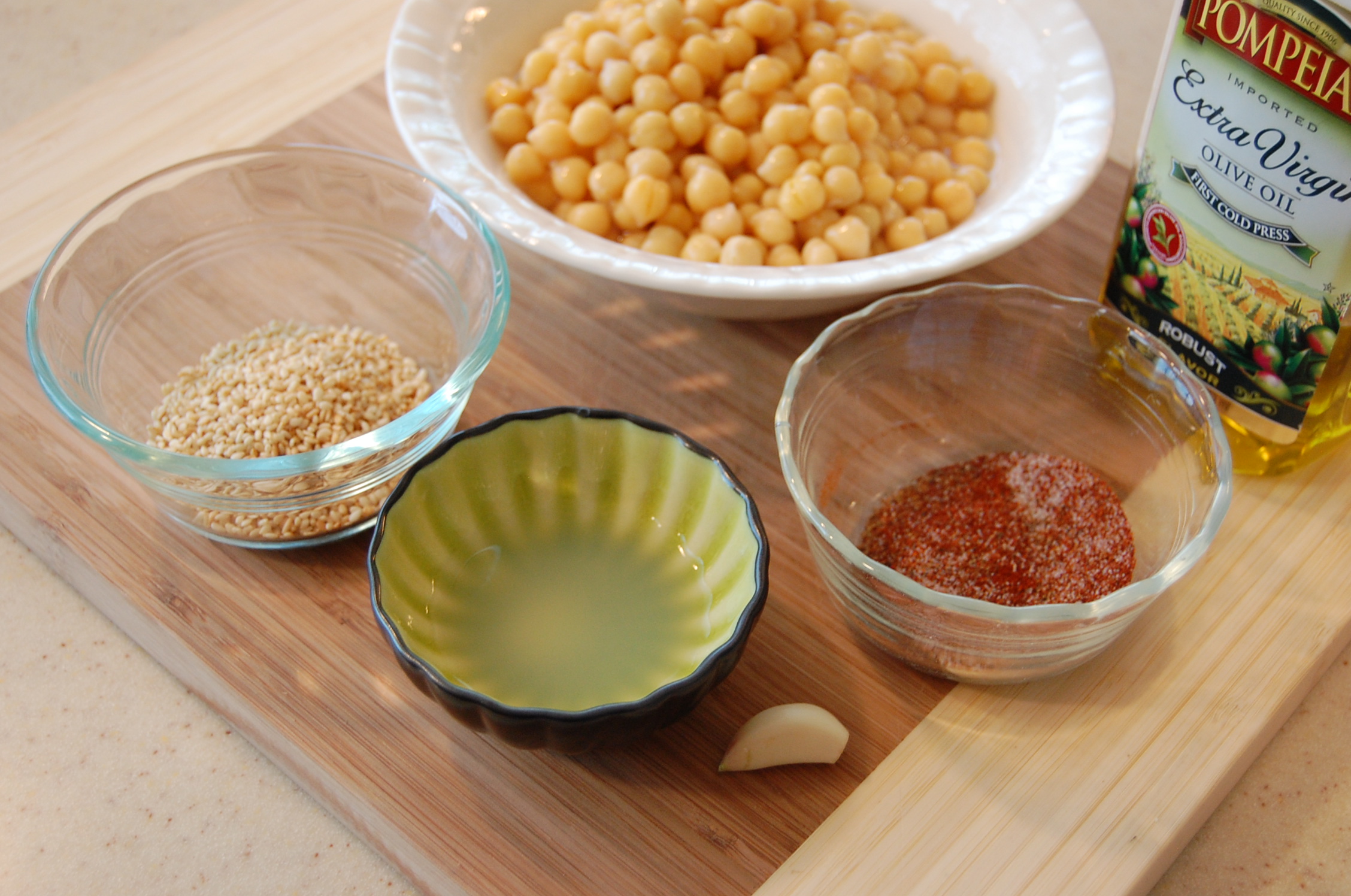 Garbanzo beans, olive oil, garlic, sesame seeds, and seasonings on a cutting board.