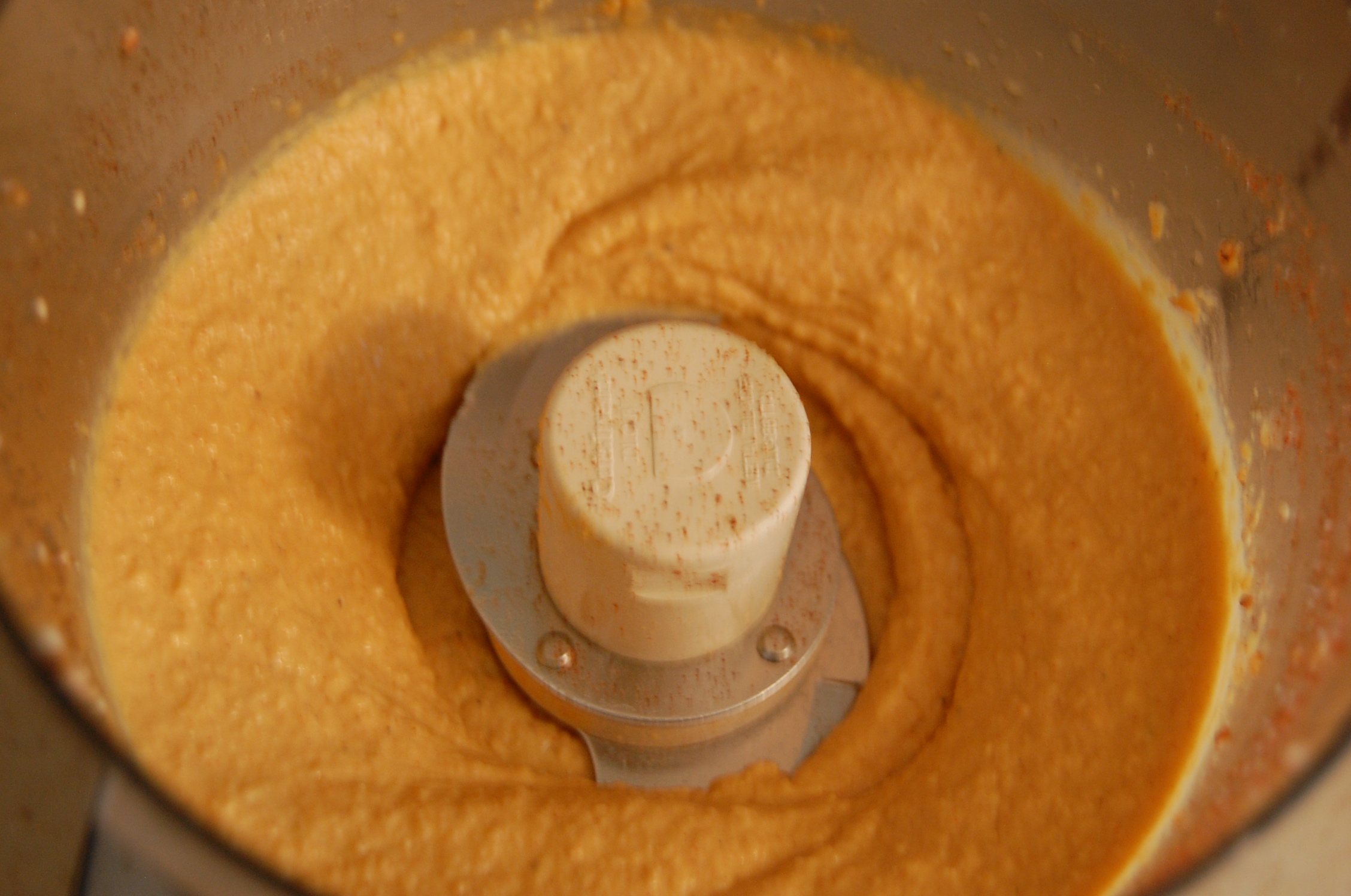 Homemade hummus being blended in the bowl of a food processor.