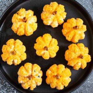 Eight mini pumpkin cheese balls on a black serving dish.